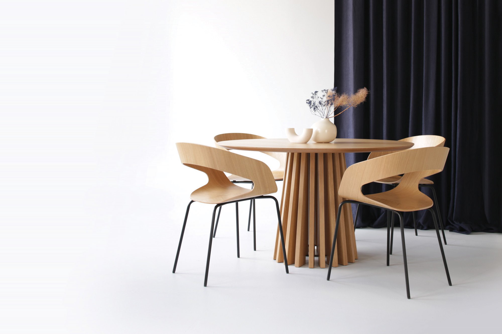 Les chaises Chat en chêne réunies autour d'une table ronde, dans un intérieur épuré ponctué d'une tenture sombre