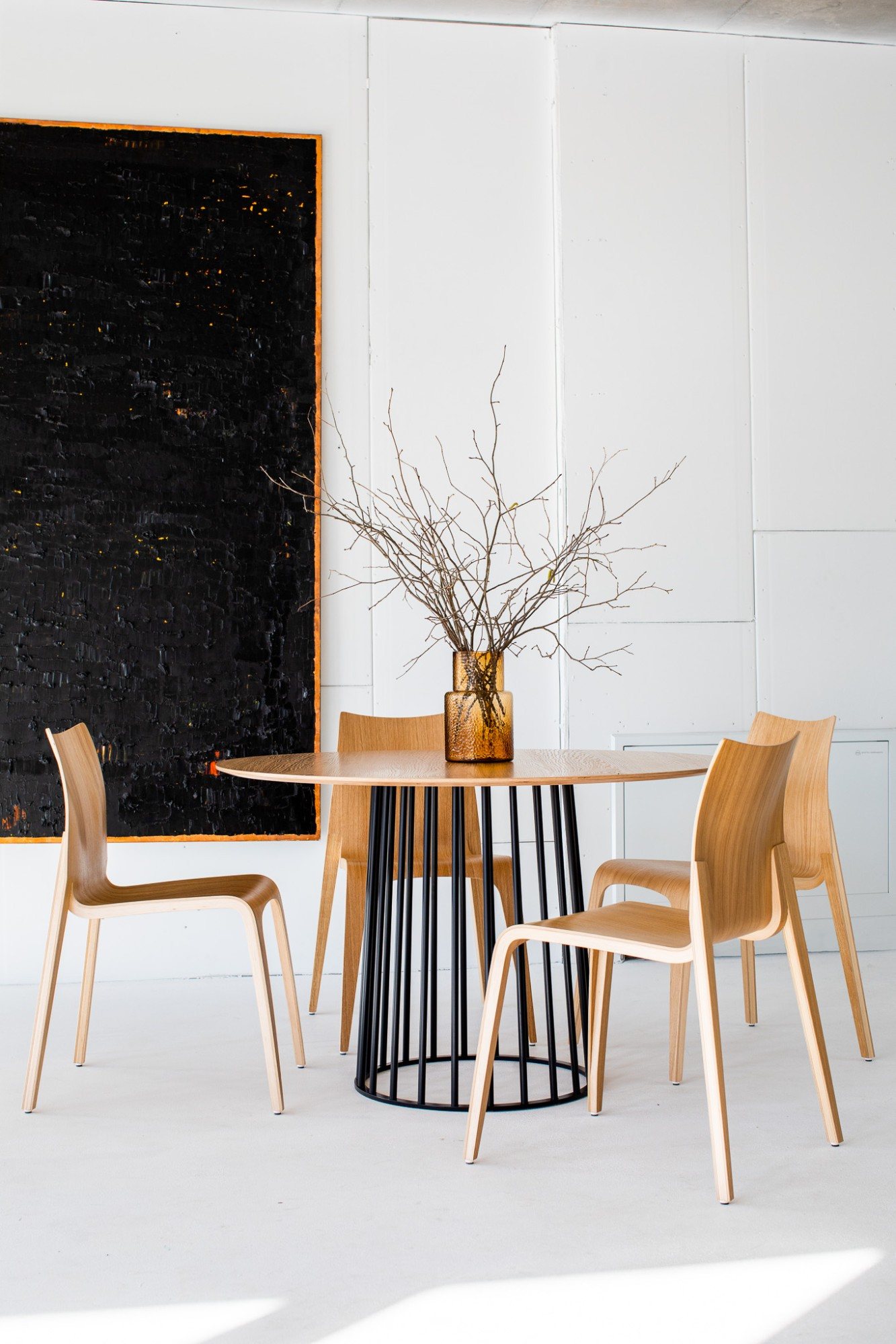 La chaise Flow en bois clair mise en scène autour d'une table ronde, dans un intérieur épuré ponctué d'une œuvre contemporaine